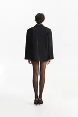 Blazer negro de silueta cuadrada, con cierre de un solo botón y solapas de satén. El cuerpo del blazer tiene un acabado brillante o de lentejuelas finas.