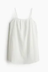 Vestido corto blanco de muselina de algodón suave, corte holgado, con breteles finos ajustables, escote recto y espalda redondeada.