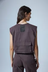 Chaleco corto color marrón confeccionado en gabardina con cierre metálico frontal, bolsillos con fuelle y badana de PU en la espalda.