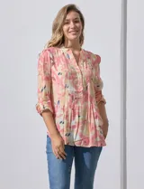 Blusa de gasa estampada con flores en tonos rosa, amarillo y azul. Tiene cuello a la base con escote en V y botones. La parte delantera tiene detalle plisado y las mangas son 3/4 regulables con presilla y botón.