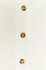 Top blanco de tejido de punto, con cuello redondo, manga larga y cierre frontal parcial con botones dorados.