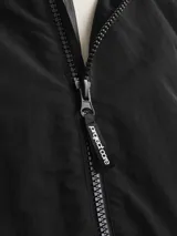 Campera negra de nylon, estilo shell, con capucha y cierre frontal con cremallera. Presenta bolsillos frontales y puños elastizados.