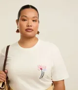 Remera de algodón color crudo, de corte alargado, con cuello redondo, mangas cortas y estampa floral con lettering Flowers Bloom en el frente.