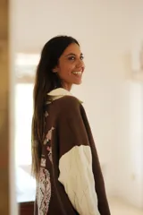 Buzo de punto en color marrón con cuello polo blanco y mangas largas blancas con textura de ochos. Presenta un diseño gráfico de gran tamaño en la espalda en tonos rosado, blanco y negro.