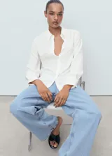 Camisa blanca de manga larga con puños abotonados, cuello camisero y cierre frontal de botones. Diseño recto con tejido fluido.