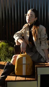 Mochila color beige con diseño capitoneado, bolsillo frontal con cierre, asa de mano y correas regulables.