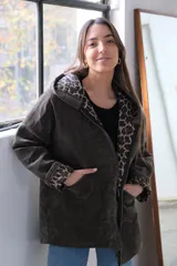 Chaqueta de pana verde con corte amplio, cierre frontal, capucha integrada y bolsillos delanteros. Interior con forro de estampado animal print.