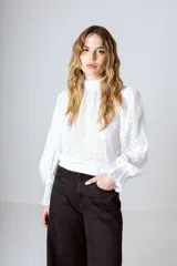 Blusa blanca de broderie con cuello alto, mangas largas abullonadas y puños elásticos.