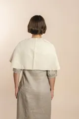 Chal asimétrico de lana color gris claro, con cortes en los hombros y doble ojal de fieltro para mantener el cruce. Terminación pespunteada y al corte.