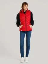 Chaleco acolchado rojo con capucha ajustable con cordones y cierre de cremallera frontal. Cuenta con bolsillos laterales con cremallera y logo de Tommy Hilfiger en el pecho.