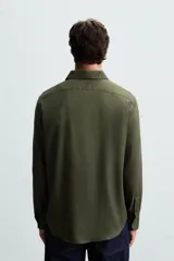 Camisa negra de manga larga con cuello italiano y cierre frontal de botonadura. Presenta un tejido con estructura de fácil cuidado.