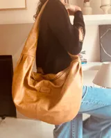 Bolso tipo hobo de cuero color camel, con correa ancha para el hombro y bolsillo interno con cierre.