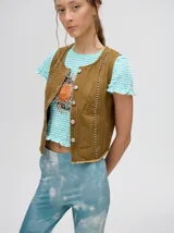 Chaleco marrón de denim con apliques metálicos y flecos en el ruedo.