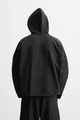 Sudadera con capucha negra, de corte oversize, confeccionada en tejido de algodón con interior en rizo. Cuenta con manga larga, bolsillos frontales tipo canguro, efecto lavado y acabados irregulares con vuelta.