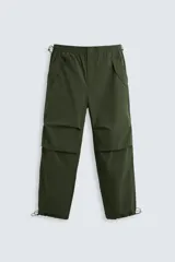 Pantalón verde militar de corte relaxed fit confeccionado en tejido técnico ligero. Cuenta con cintura elástica ajustable con cordón interior, bolsillos frontales y traseros con solapa, pliegues en las rodillas y bajo ajustable con elástico.