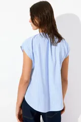 Blusa celeste a rayas verticales blancas, de corte holgado, manga corta y cuello mao con escote en V.