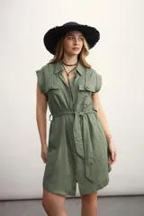 Vestido camisero corto color verde oliva, con cuello clásico, mangas cortas con charreteras, cierre frontal con botones y cinturón de lazo. Presenta bolsillos con solapa en el pecho y bolsillos laterales.