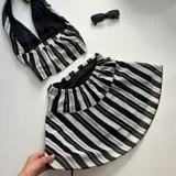 Conjunto de moda que incluye top tipo halter y falda corta a rayas en blanco y negro, acompañado de un bolso negro y botas altas.