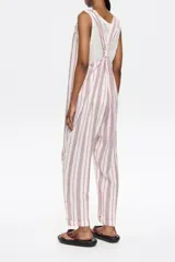 Mono largo de lino color crudo con rayas verticales rojas y azules. Tiene corte recto, escote redondeado pronunciado, tirantes anchos con trabillas para fruncir y espalda nadadora.