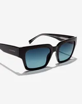 Lentes de sol unisex Hawkers, modelo Mate, con montura cuadrada negra y cristales degradados de azul a transparente.