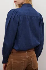 Camisa azul marino con estampado floral en color lila, cuello mao con volantes, cierre frontal de botones y mangas largas abullonadas con puños elásticos.