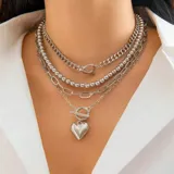 Set de cuatro collares plateados de diferentes estilos: cadena de eslabones gruesos, cadena de eslabones de bolitas, cadena de eslabones ovalados y una cadena más fina con un dije de corazón tridimensional con cierre tipo toggle.