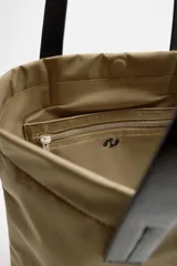 Bolso tipo shopper color beige, fabricado en tejido técnico con asas de mano de cuero negro. Tiene compartimento principal con cierre magnético y bolsillo interior con cremallera.