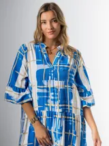Vestido midi de corte amplio con estampado abstracto en tonos azules, blancos y beige. Tiene cuello en V, mangas 3/4 con volados y corte escalonado en la falda.