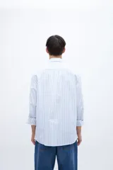 Camisa celeste con rayas verticales blancas, de corte regular, con cuello solapa clásico, bolsillo en el pecho y botones personalizados.