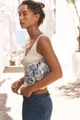 Bolso de mano tipo clutch con cuerpo cubierto de abalorios en tonos beige, azul y gris. Tiene un diseño floral y un cierre imantado. Incluye correa metálica extraíble y bolsillo interior con cremallera.
