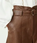 Short marrón de cuero sintético, tiro alto, corte clochard, con cinturón con hebilla metálica.