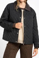 Campera capitoneada de color negro con diseño de rombos, cuello camisero en contraste de color marrón, cierre frontal con cremallera y solapa con botones a presión. Presenta mangas largas con puños ajustables y un calce entallado.