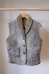 Chaleco gris de cuero con cuello solapa, cierre con botones y bolsillos frontales.