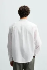 Camisa de algodón blanco con efecto arrugado, cuello mao (tira) y manga larga con puño abotonado. Presenta un corte relajado (relaxed fit) y cierre frontal de botonadura.