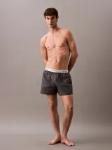 Bóxer suelto de hombre Calvin Klein, confeccionado en popelín de algodón con estampado de logos en gris y cintura elástica blanca con logo.