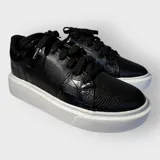 Championes negros de cuero sintético con textura tipo piel de reptil, cordones anchos y suela plana.