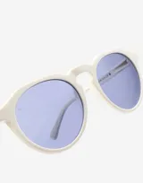 Lentes de sol Hawkers unisex, modelo Warwick Raw, con montura color marfil y lentes celestes.