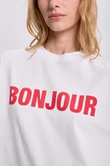 Remera blanca de corte boxy con estampa roja de la palabra "Bonjour" en el frente.