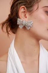 Aros tipo caravana grandes con forma de moño, completamente cubiertos de strass plateado.