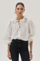 Blusa blanca con lunares en relieve, cuello con volados y lazos, mangas abullonadas 3/4 y bordados con lentejuelas en el frente.