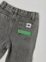 Pantalón jean gris con corte recto, bolsillos delanteros y traseros, pretina elástica y cintas cosidas de colores en los laterales y en la parte inferior delantera.