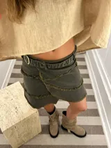 Minifalda tipo portafolio de denim color verde oscuro/gris, con borde deshilachado y ajuste lateral con tira y ojalillos metálicos.