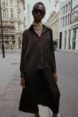 Camisa oversize color marrón oscuro confeccionada en tejido satinado con efecto arrugado, cuello solapa, manga larga con puños y cierre frontal con botones metálicos.