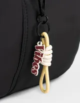 Cartera saca negra de tela deportiva con correa regulable, cierre superior y bolsillo frontal con cierre. Incluye charm lateral.