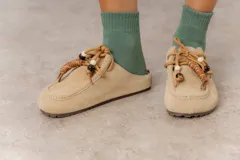 Zueco de cuero gamuzado color beige, con cordones decorativos con cuentas y piezas envueltas en cuero. Tiene plantilla acolchada y base liviana.