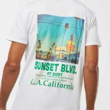 Camiseta blanca de manga corta con estampado verde de texto "L.A. California Sunset Blvd.".