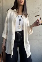 Camisa beige con bordados florales blancos, de corte recto y mangas largas con puños enrollados.