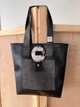 Bolso tote negro con textura símil cuero de cocodrilo, con bolsillo externo decorativo y cierre con botón metálico.