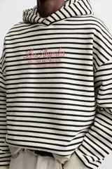 Sudadera con capucha a rayas horizontales blancas y negras, corte boxy fit, mangas largas y texto bordado en color rosa en el pecho.
