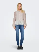 Blusa blanca con textura de lunares, cuello con volantes y lazo, cierre frontal con botones, mangas largas abullonadas con puños elásticos y corte peplum.